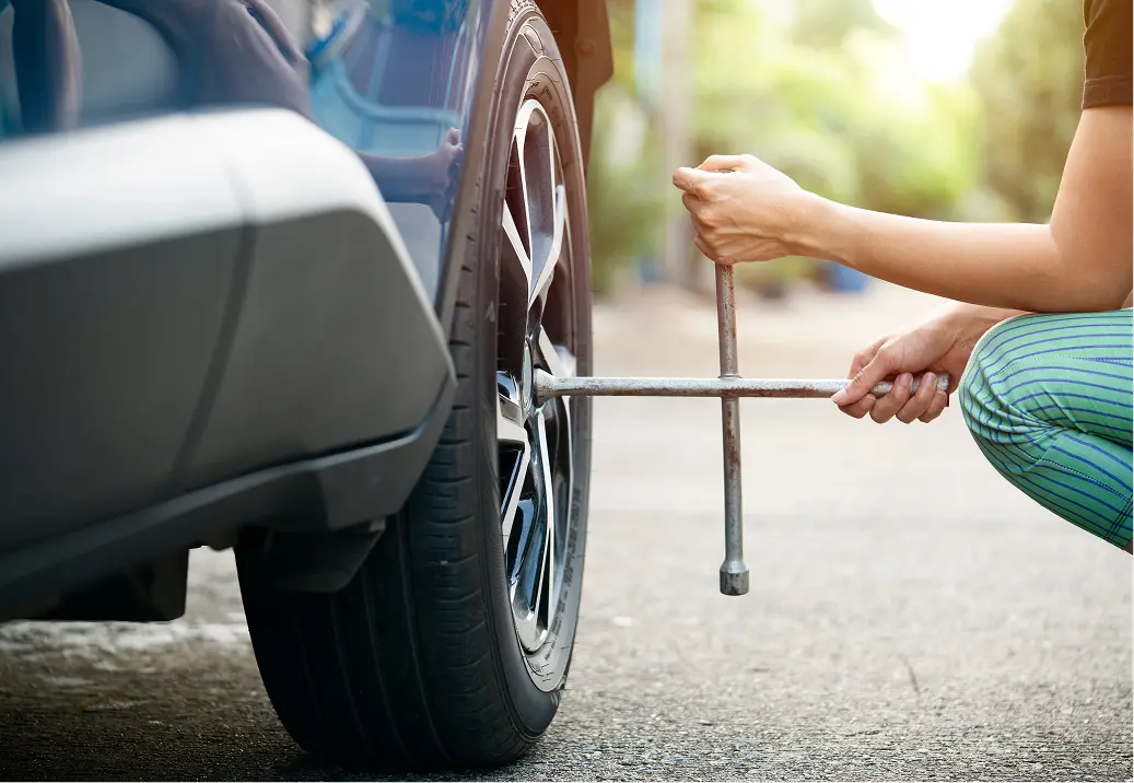 Person changing car tire with wrench.
