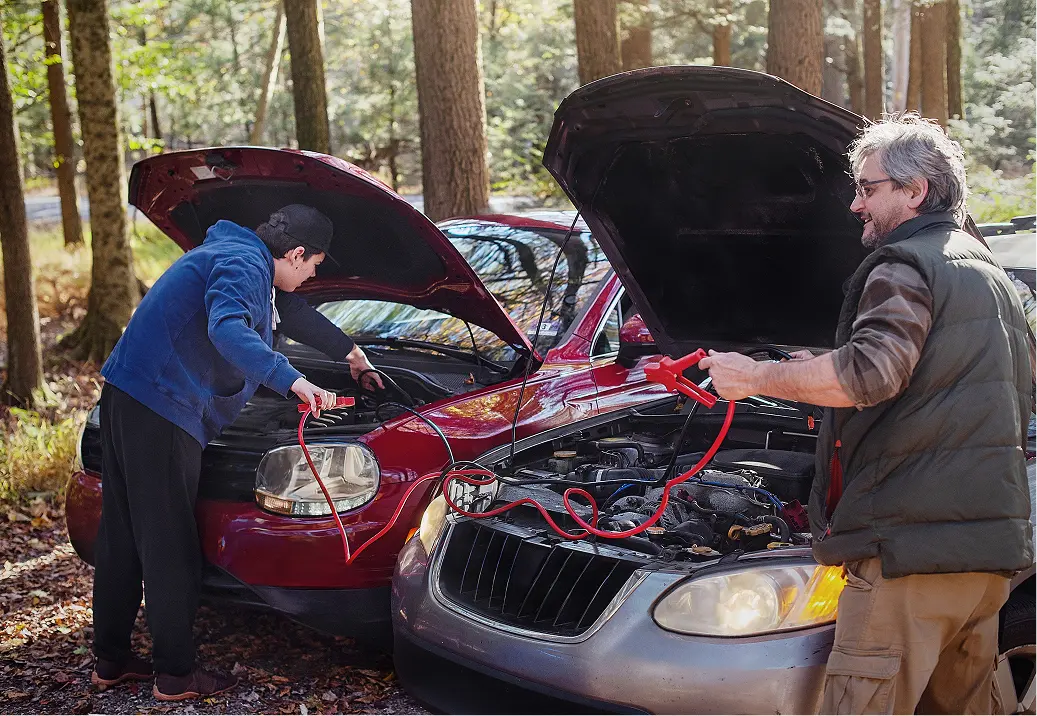 Two men jump-starting a car in woods.