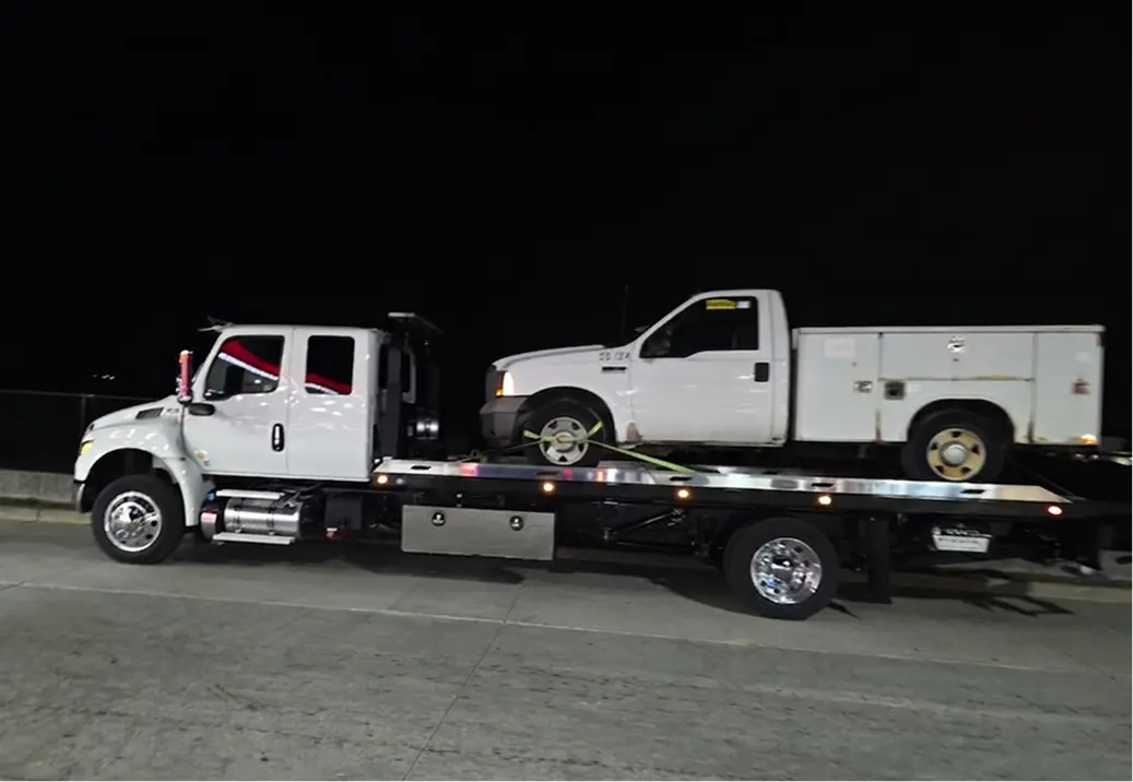 Tow truck carrying a white utility truck.